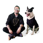 Perro de raza grande negro y blanco con sudadera con gorro negra y diseño dorado y humano con sudadera que combina.
